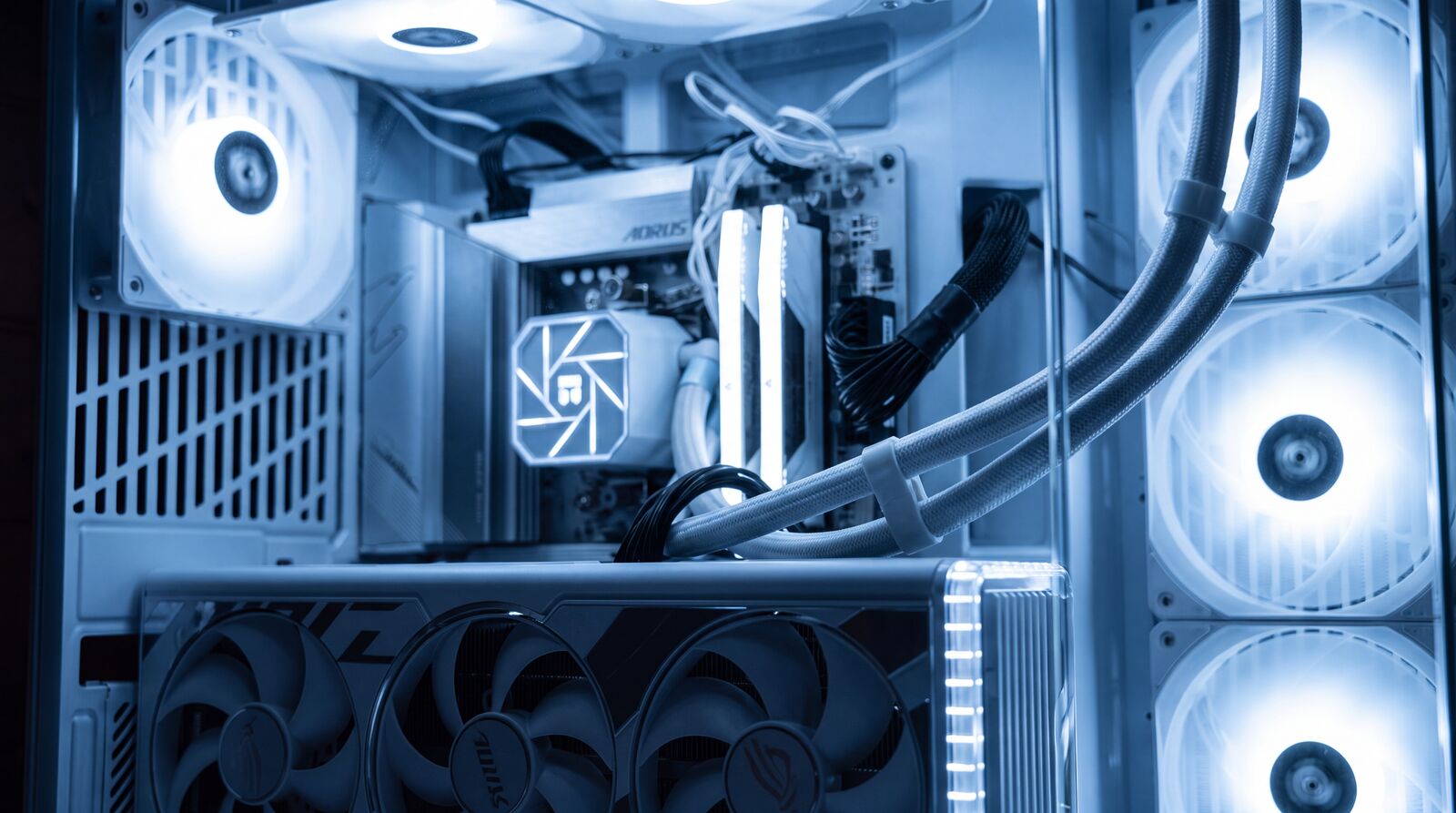 Innenansicht eines selbst gebauten PCs: weisses Mainboard, Wasserkühlung und gesleevte Kabel im kalten Licht